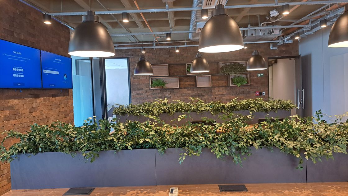 Sala de reunião de escritório corporativo reformado pela Vallim: parede de tijolos, jardim vertical e mesa de madeira